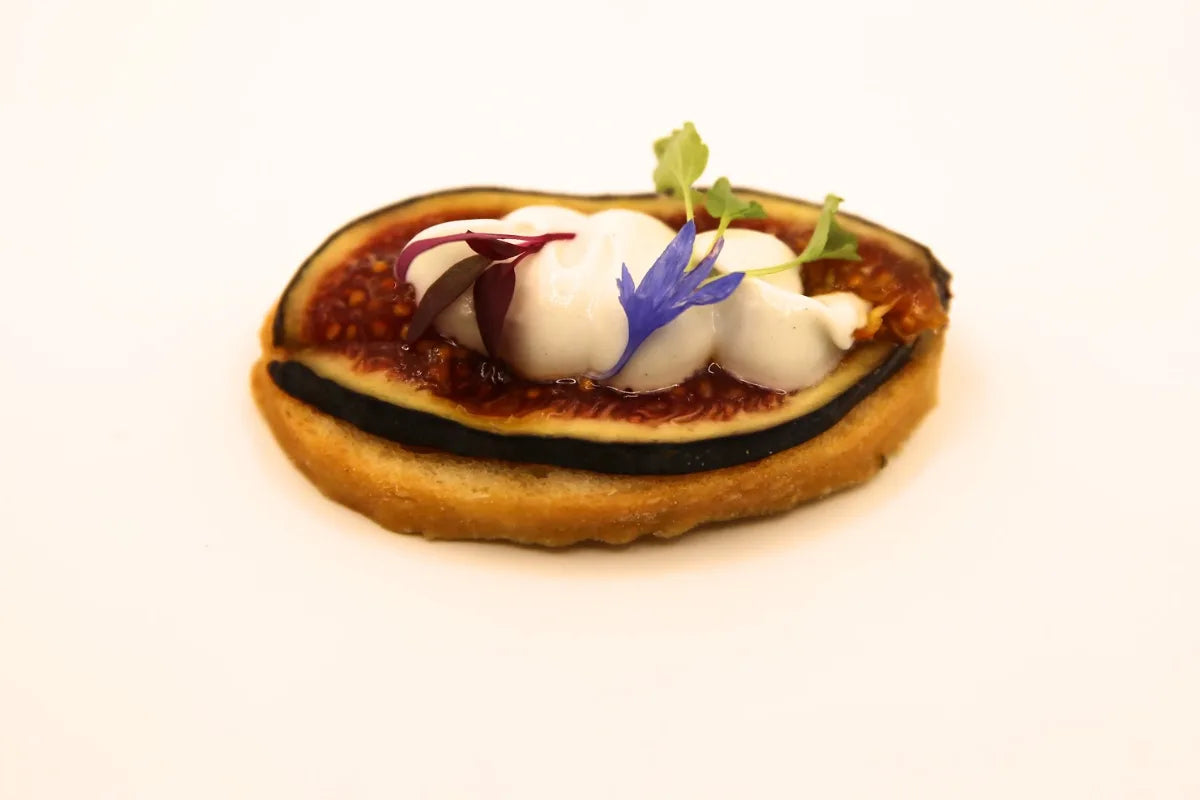 Canapé of fig and whipped cheese on a crisp base, finished with cornflower petals and micro herbs