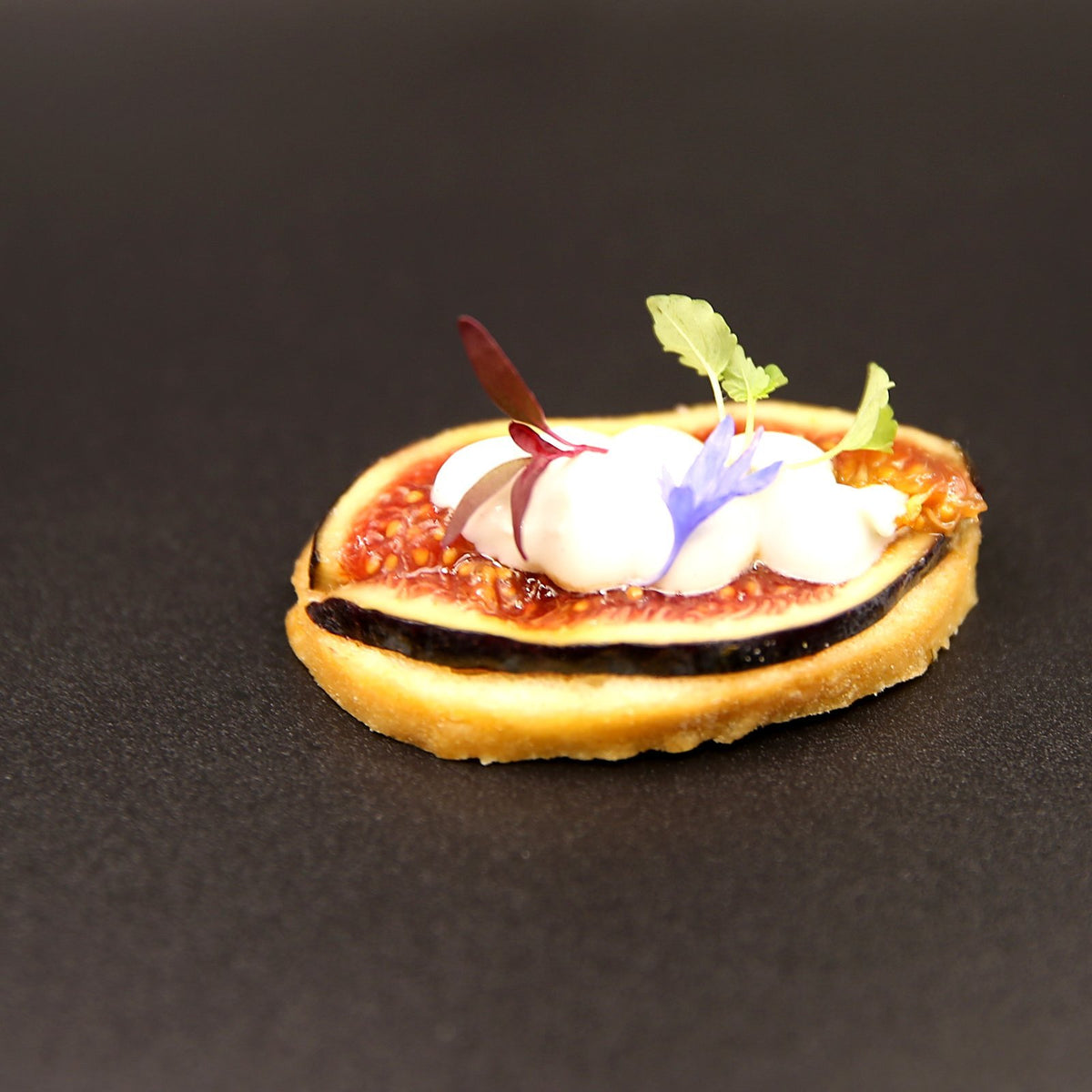Fresh fig slice on crisp crostini topped with whipped goat's cheese and cornflower petals