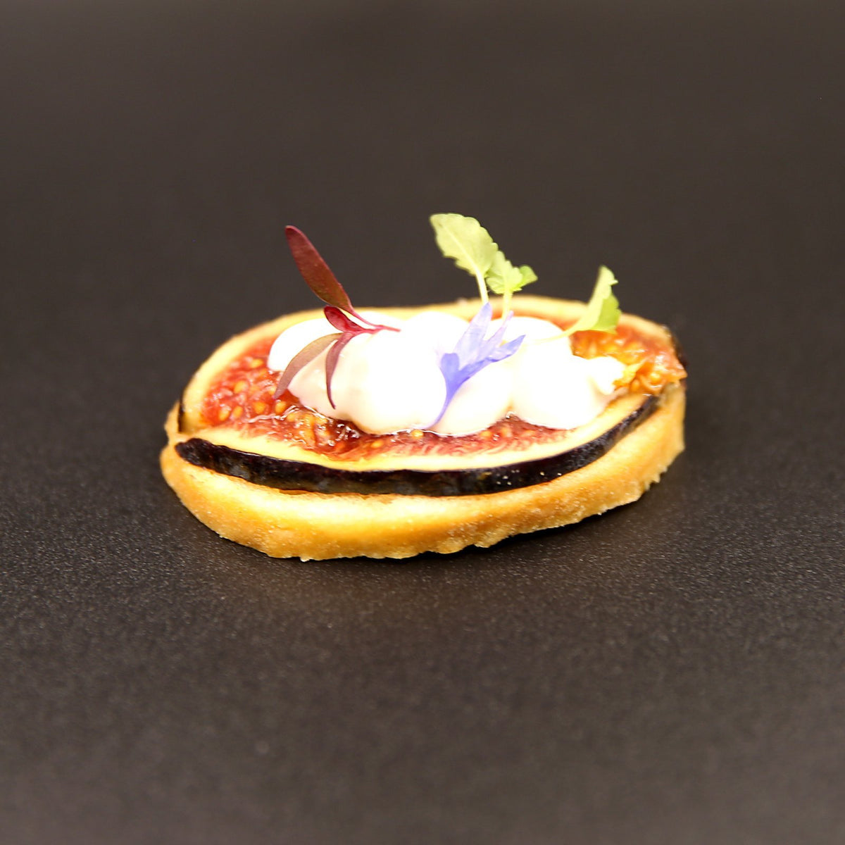 Goat's cheese and fresh fig crostini canapé garnished with edible flowers and micro herbs