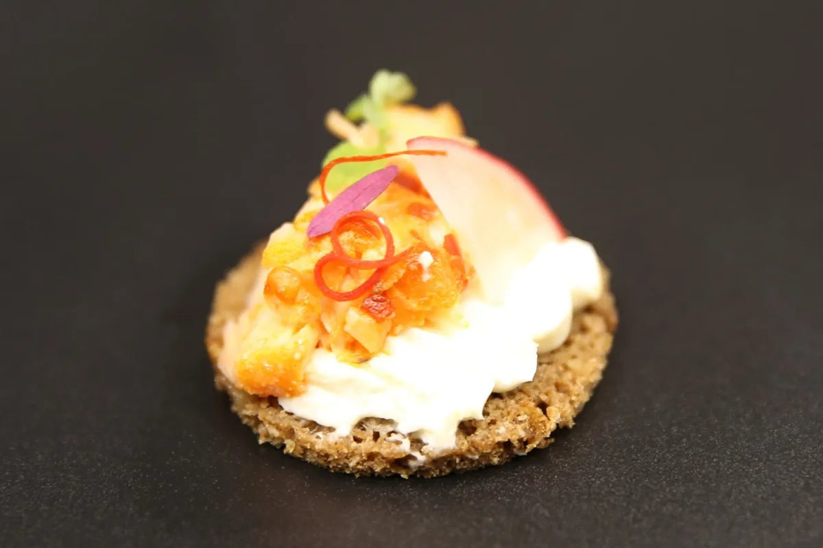 Rye crisp canapé topped with whipped cheese, chilli, shaved radish and micro herbs