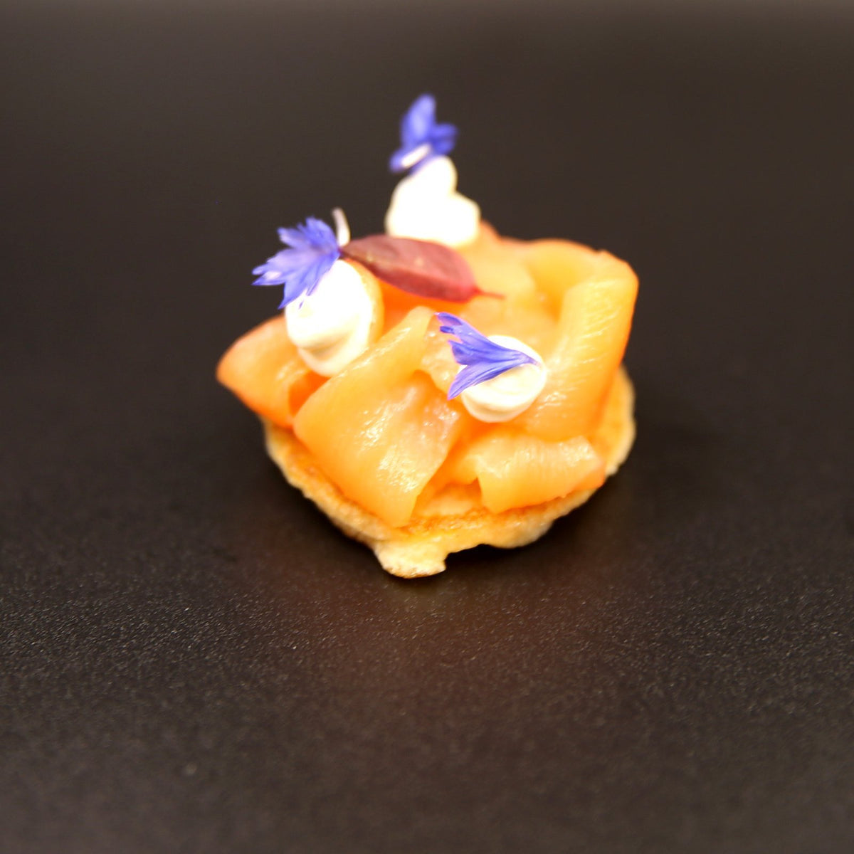 Smoked salmon blini canapé topped with crème fraîche, edible cornflowers and micro herbs, delivered in London