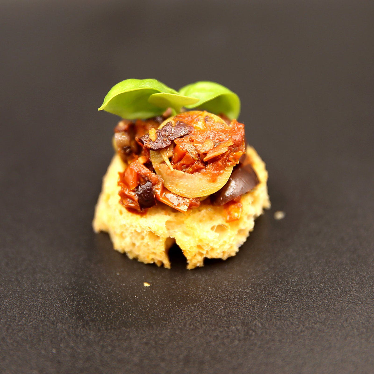 Close-up of tomato and olive tapenade on tomato bread canapé with basil leaves