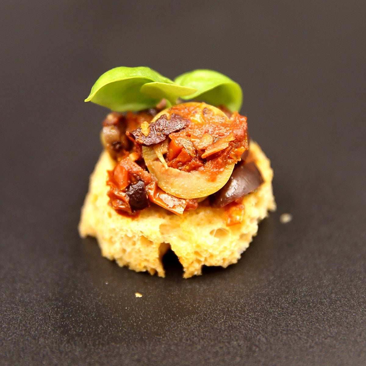 Tomato tapenade canapé with olives and sun-dried tomato on toasted tomato bread, topped with fresh basil