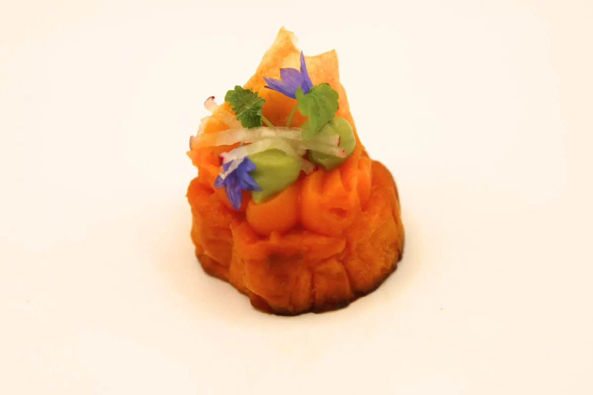 Small vegetable timbale canapé topped with avocado, herbs and blue cornflower petals